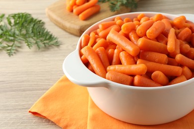 Photo of Baby carrots in pot and green leaves on wooden table