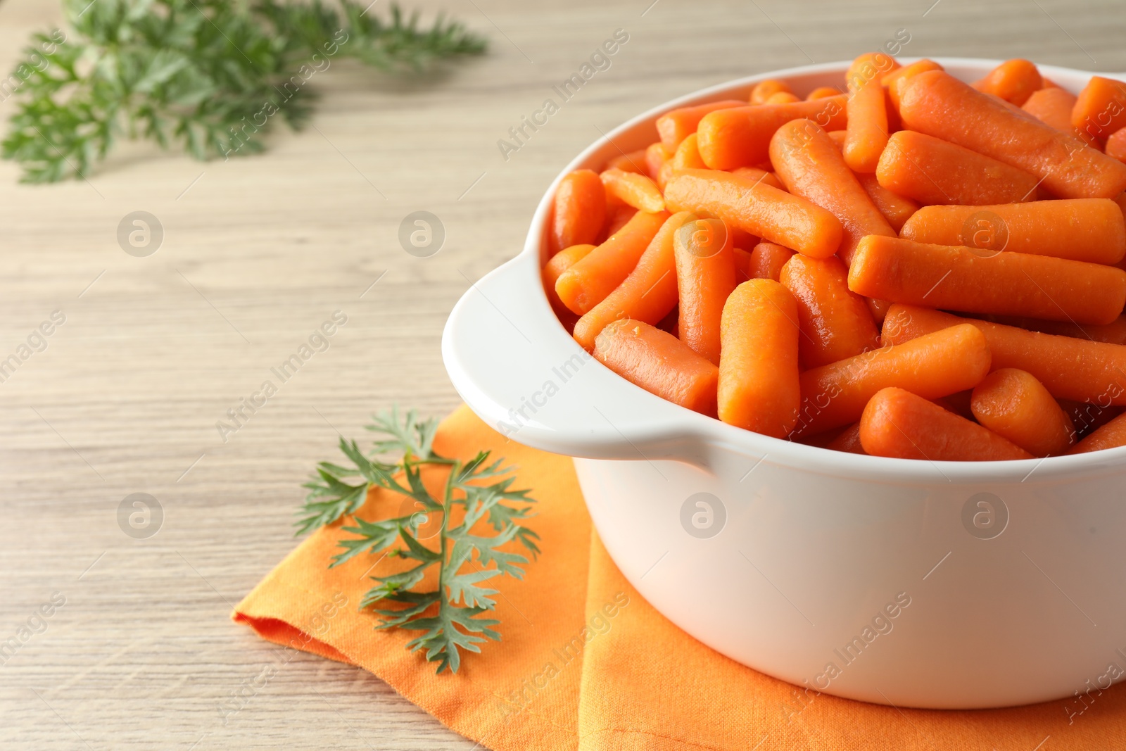 Photo of Baby carrots in pot and green leaves on wooden table. Space for text