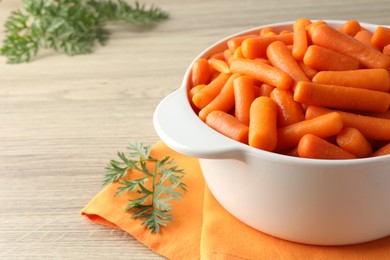 Baby carrots in pot and green leaves on wooden table. Space for text