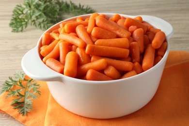 Baby carrots in pot and green leaves on wooden table