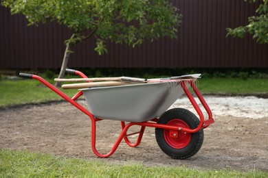 Wheelbarrow with rake and shovel outdoors. Gardening tools