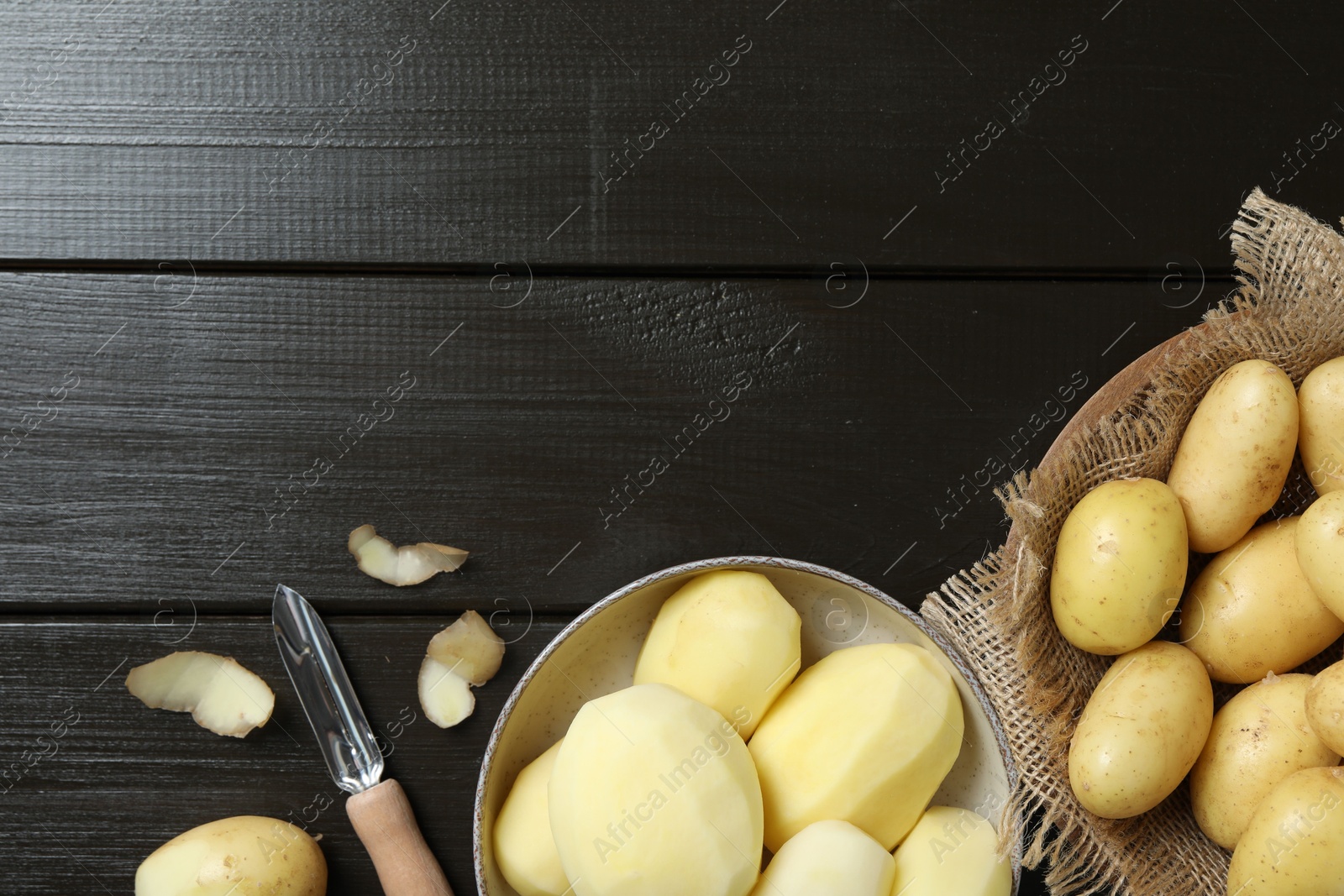 Photo of Fresh raw potatoes and peeler on black wooden table, flat lay. Space for text