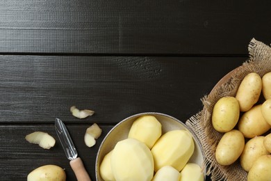 Fresh raw potatoes and peeler on black wooden table, flat lay. Space for text