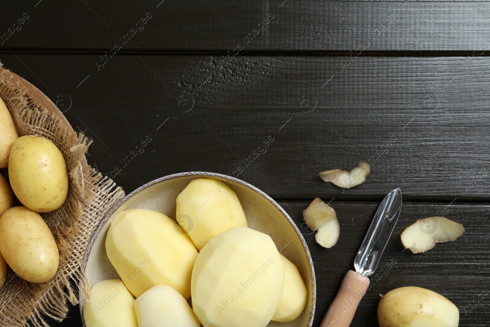 Photo of Fresh raw potatoes and peeler on black wooden table, flat lay. Space for text