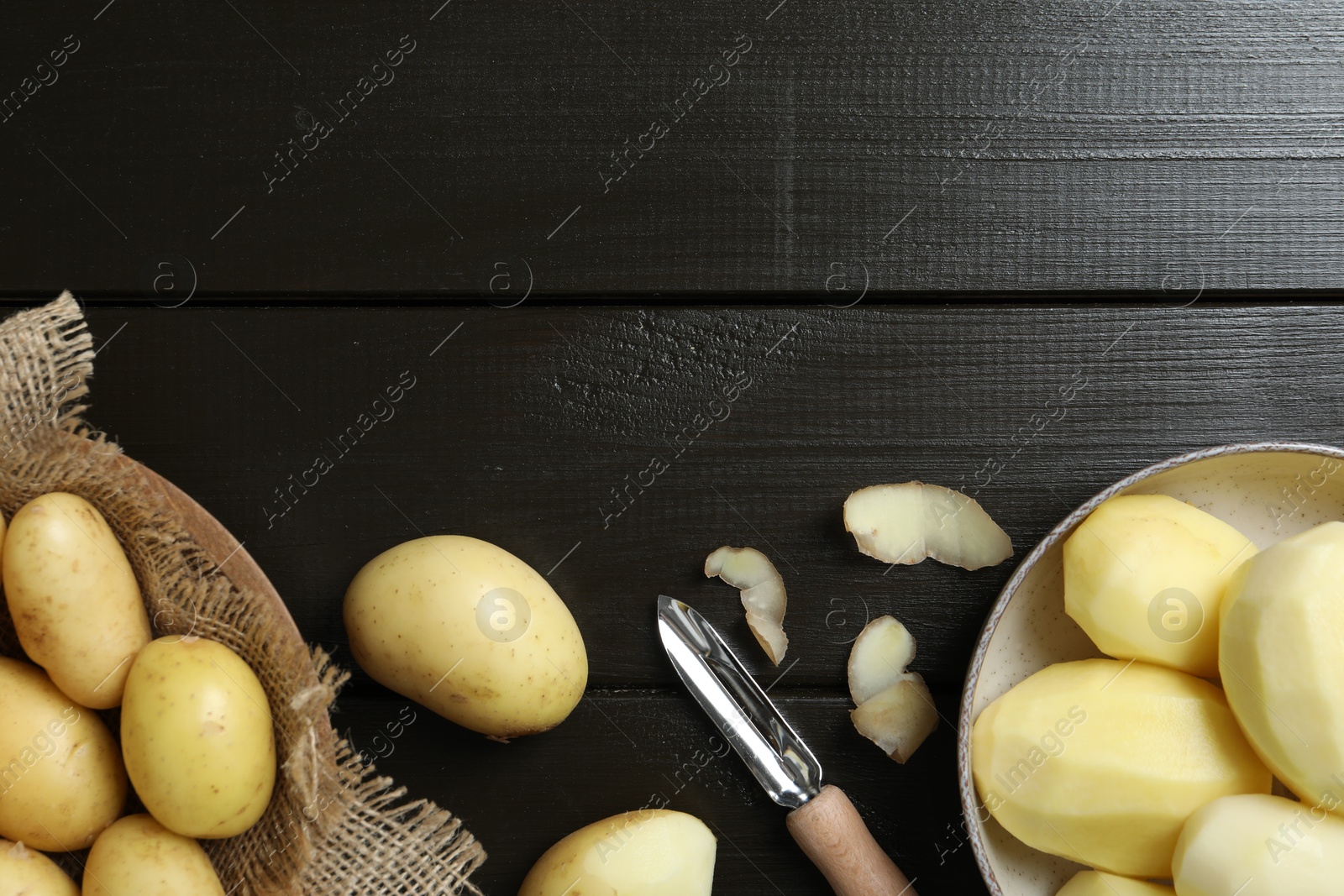 Photo of Fresh raw potatoes and peeler on black wooden table, flat lay. Space for text