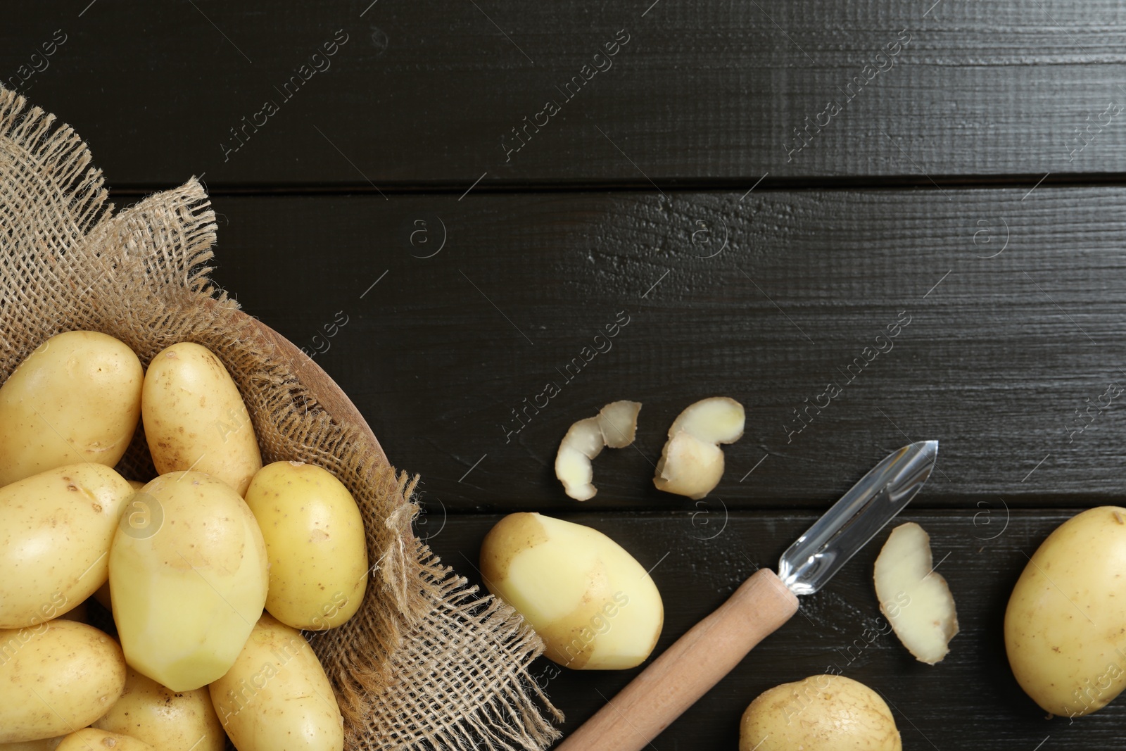 Photo of Fresh raw potatoes and peeler on black wooden table, flat lay. Space for text