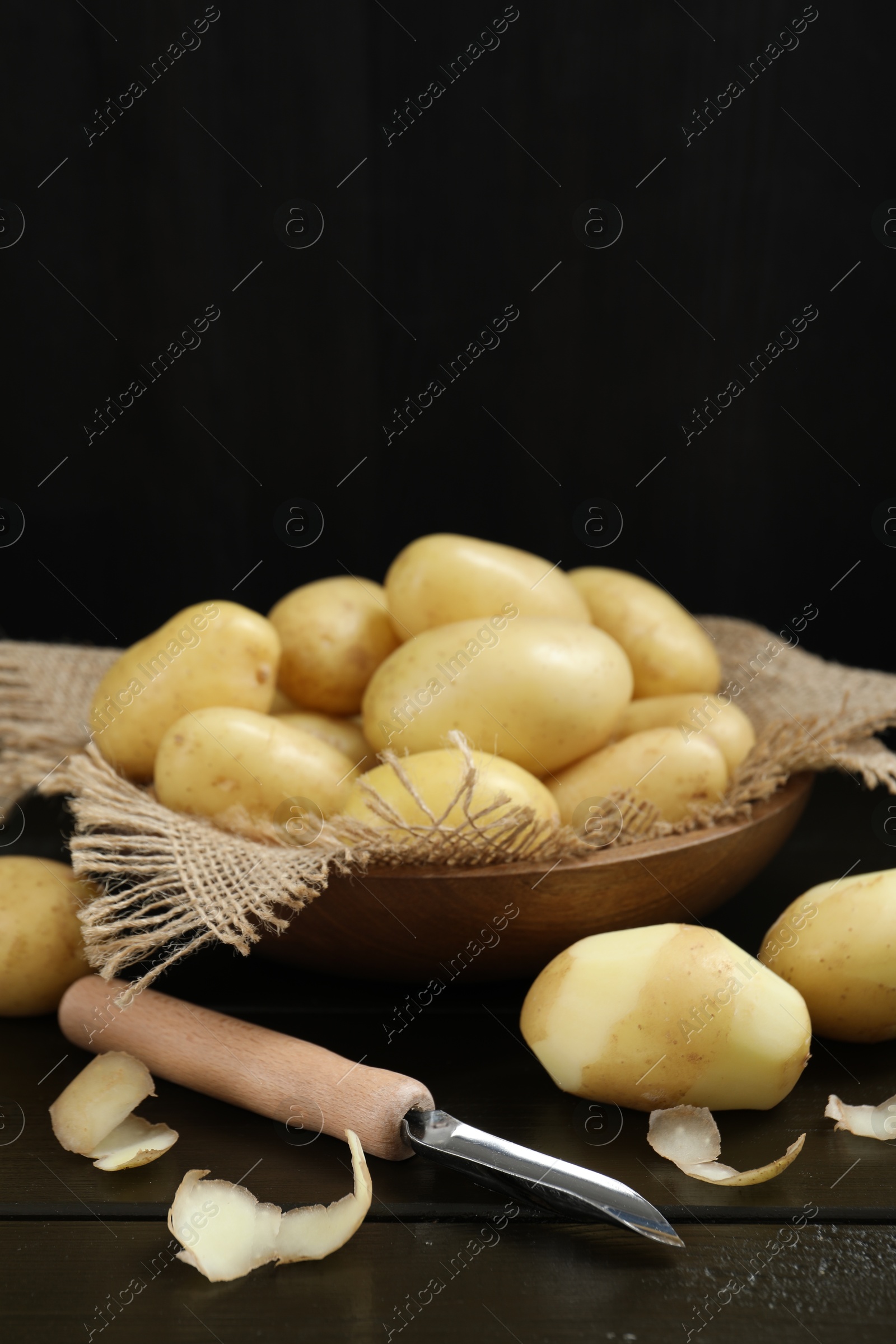 Photo of Fresh raw potatoes and peeler on black wooden table