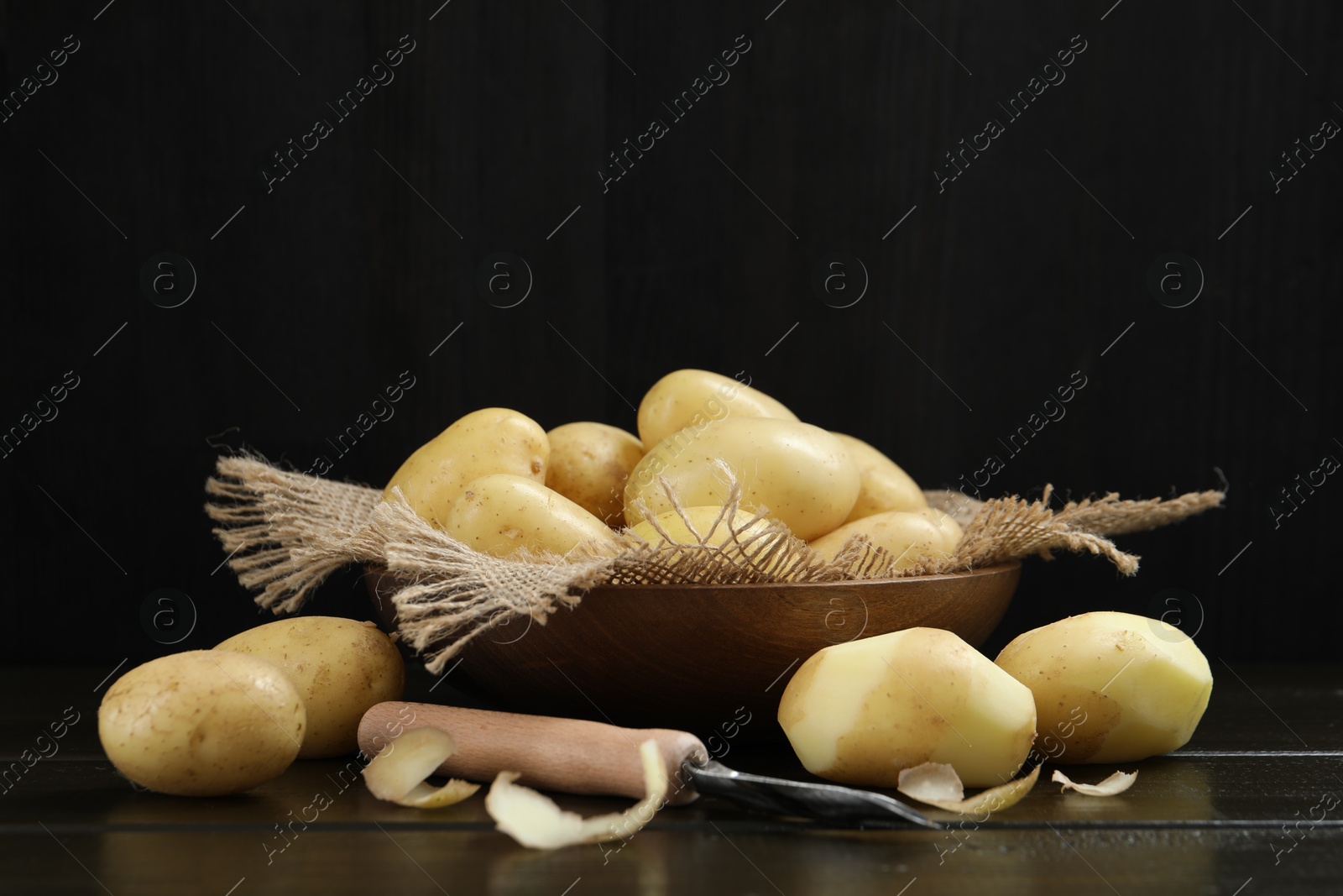 Photo of Fresh raw potatoes and peeler on black wooden table