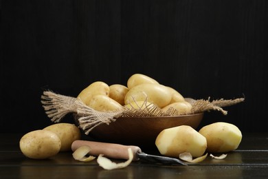 Photo of Fresh raw potatoes and peeler on black wooden table