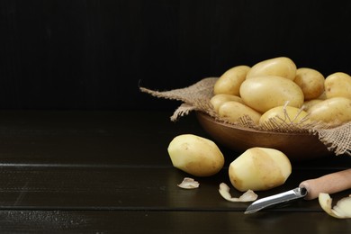 Photo of Fresh raw potatoes and peeler on black wooden table. Space for text