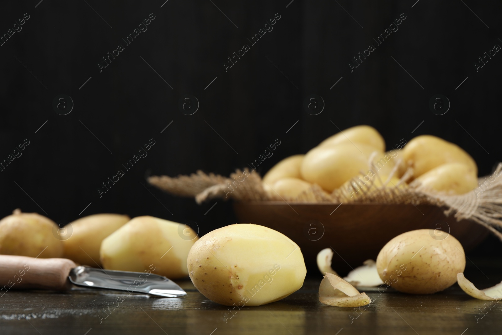 Photo of Fresh raw potatoes and peeler on black wooden table