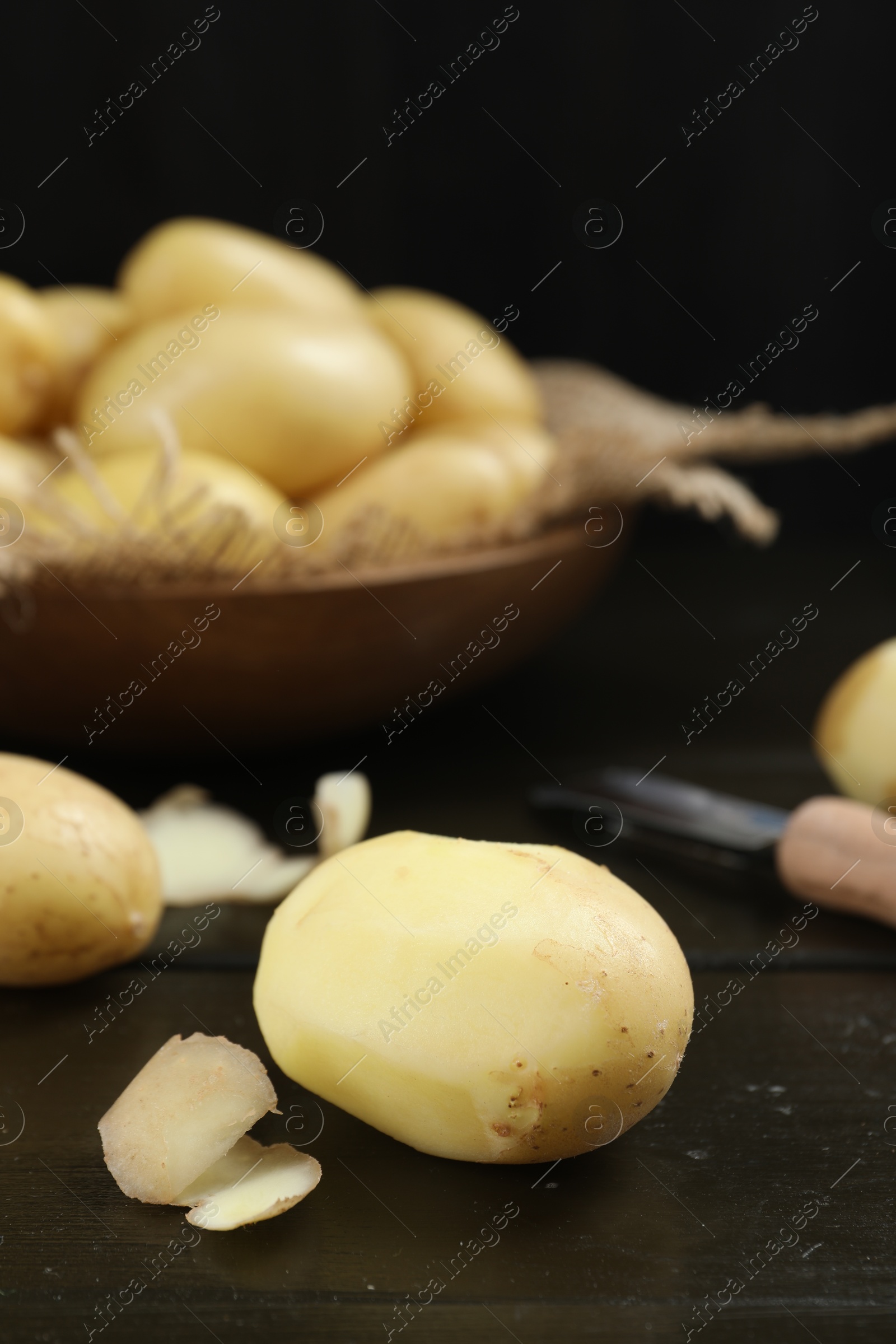 Photo of Fresh raw potatoes and peeler on black wooden table, closeup