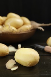 Fresh raw potatoes and peeler on black wooden table, closeup