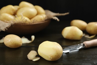 Photo of Fresh raw potatoes and peeler on black wooden table, closeup