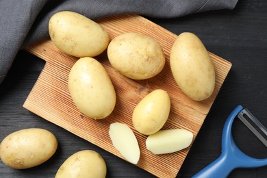 Fresh raw potatoes and peeler on black wooden table, flat lay