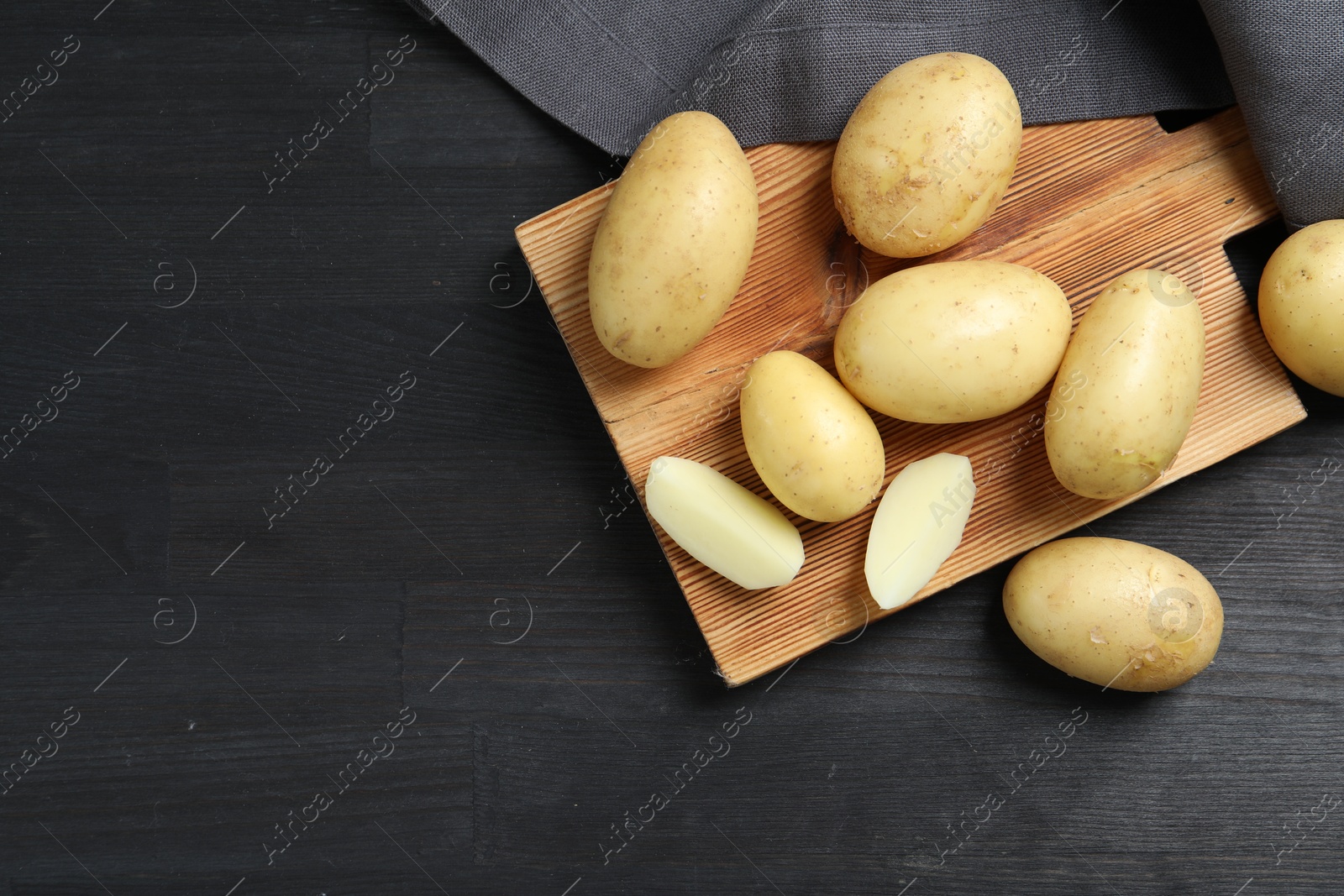 Photo of Fresh raw potatoes and cutting board on black wooden table. Space for text