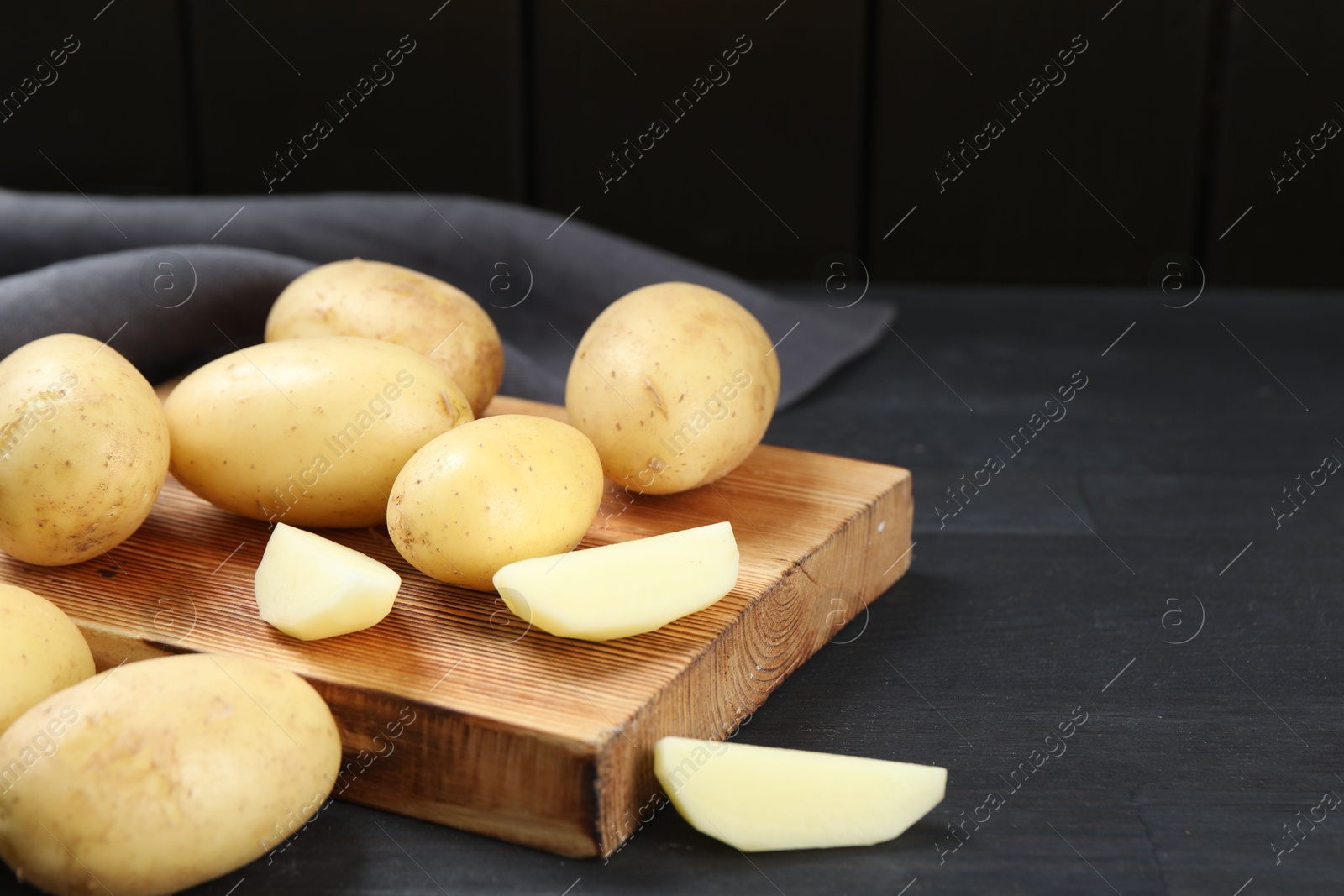 Photo of Fresh raw potatoes and cutting board on black wooden table. Space for text