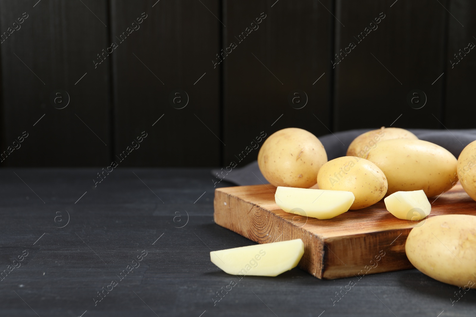 Photo of Fresh raw potatoes and cutting board on black wooden table. Space for text