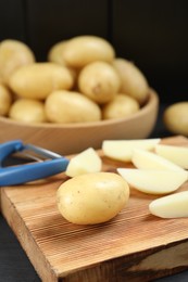 Photo of Fresh raw potatoes and peeler on black wooden table