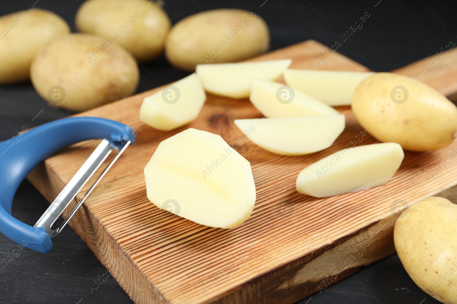 Photo of Fresh raw potatoes and peeler on black wooden table, closeup