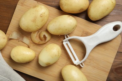 Fresh raw potatoes and peeler on wooden table, flat lay