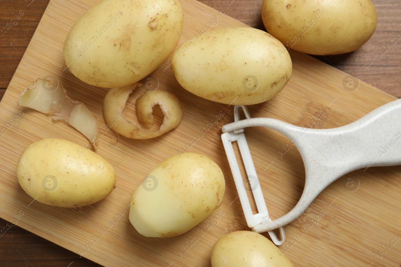 Photo of Fresh raw potatoes and peeler on wooden table, flat lay