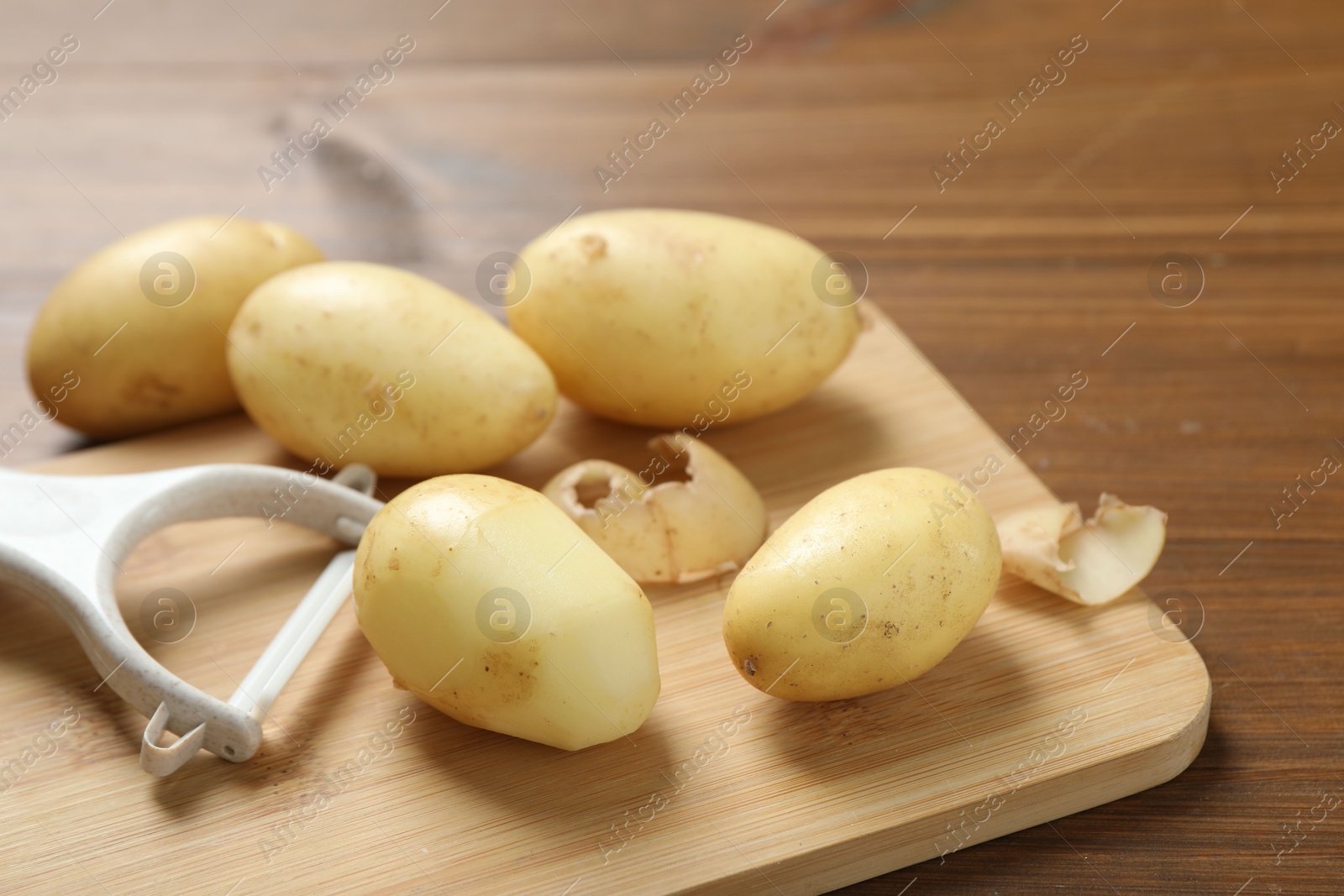 Photo of Fresh raw potatoes and peeler on wooden table, closeup