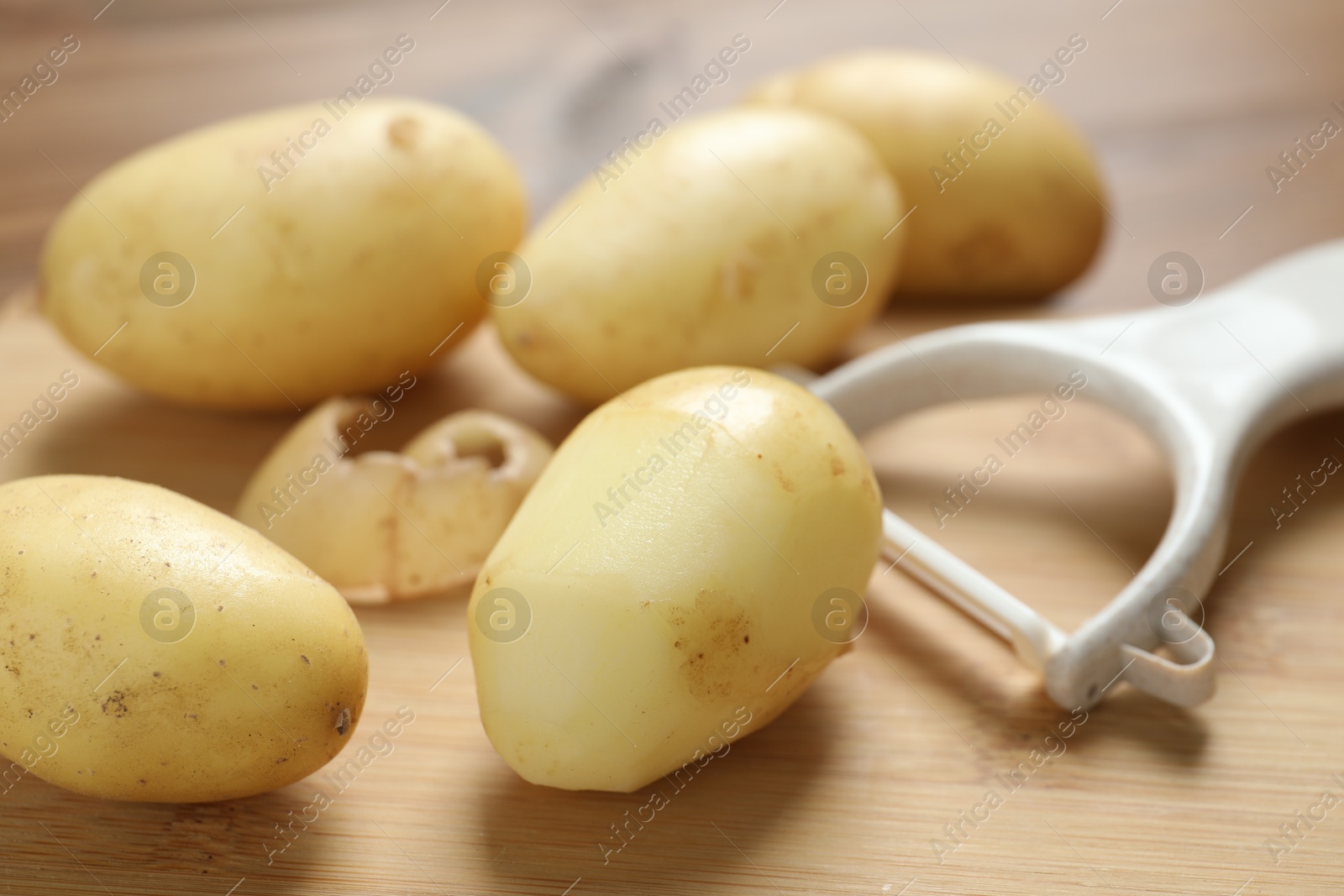 Photo of Fresh raw potatoes and peeler on wooden table, closeup