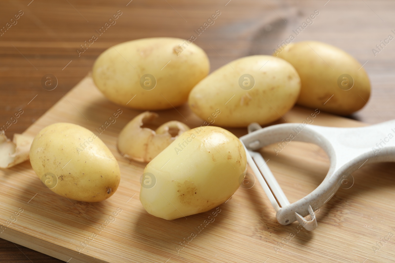 Photo of Fresh raw potatoes and peeler on wooden table, closeup