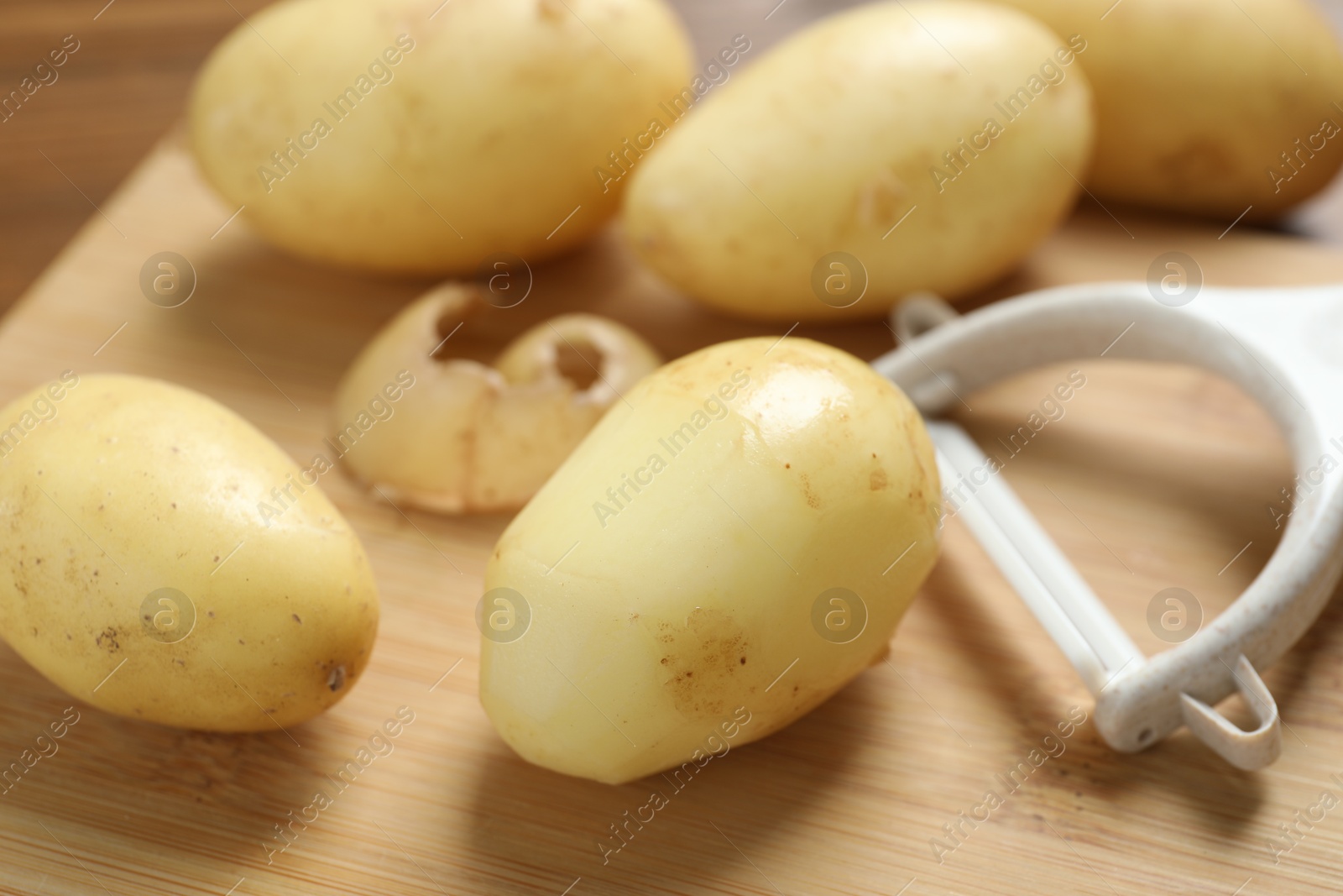 Photo of Fresh raw potatoes and peeler on wooden table, closeup