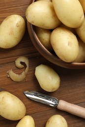 Fresh raw potatoes and peeler on wooden table, flat lay