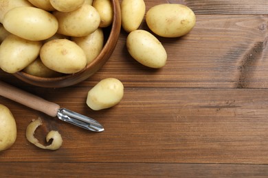 Photo of Fresh raw potatoes and peeler on wooden table, flat lay. Space for text