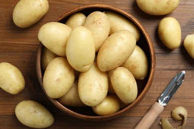 Fresh raw potatoes and peeler on wooden table, flat lay