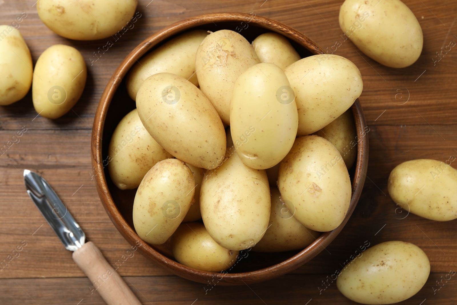 Photo of Fresh raw potatoes and peeler on wooden table, flat lay