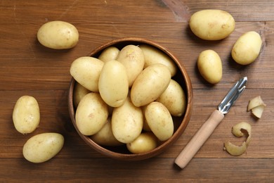 Photo of Fresh raw potatoes and peeler on wooden table, flat lay