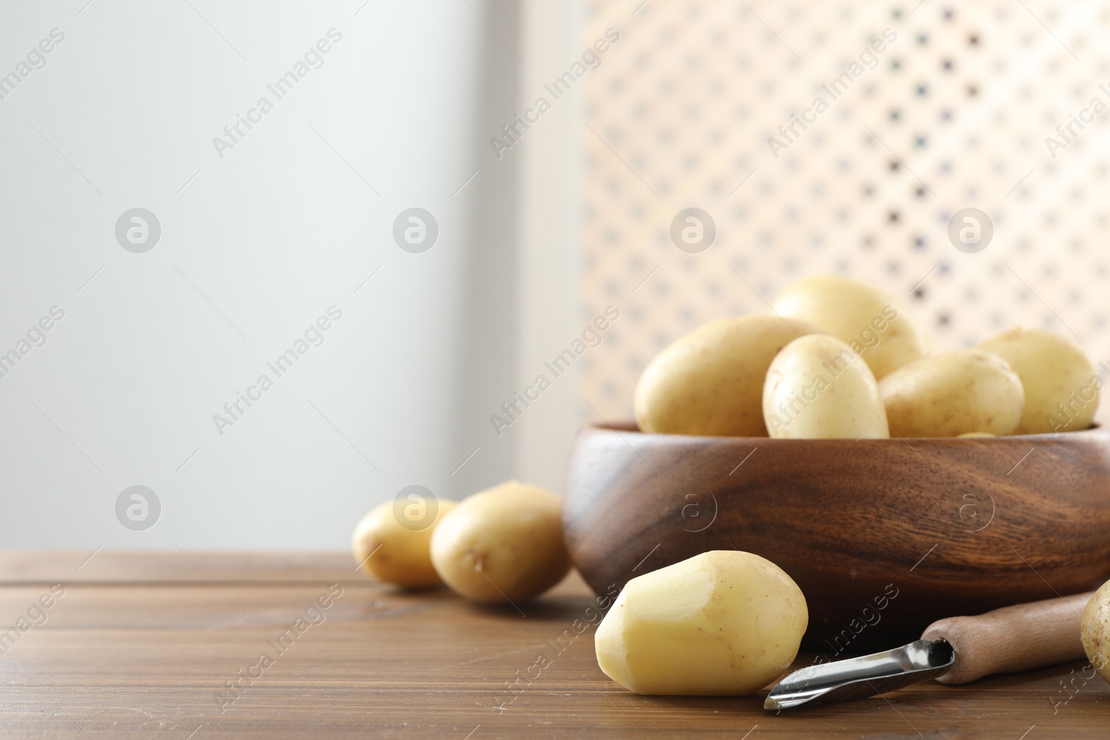 Photo of Fresh raw potatoes and peeler on wooden table. Space for text