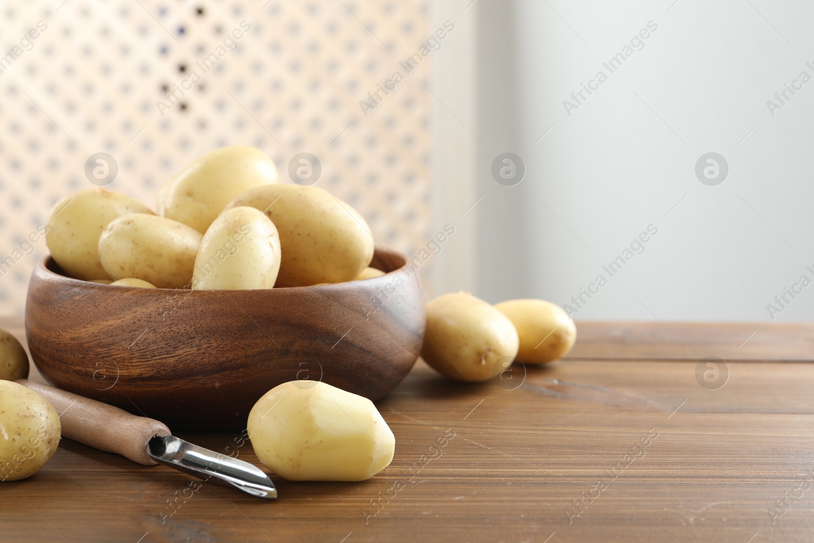 Photo of Fresh raw potatoes and peeler on wooden table. Space for text