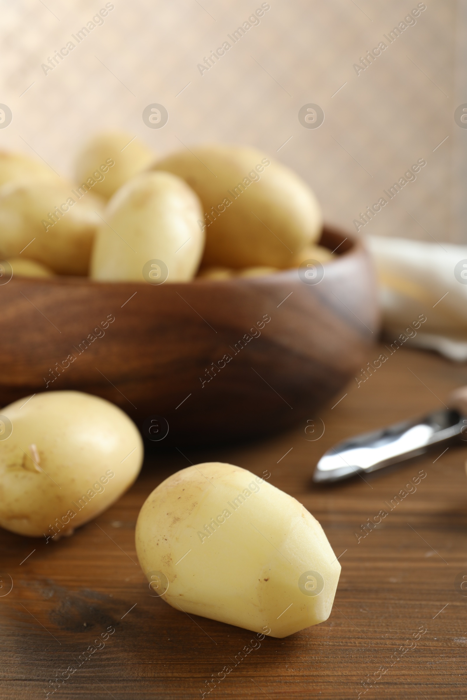 Photo of Fresh raw potatoes and peeler on wooden table, closeup