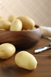 Photo of Fresh raw potatoes and peeler on wooden table, closeup