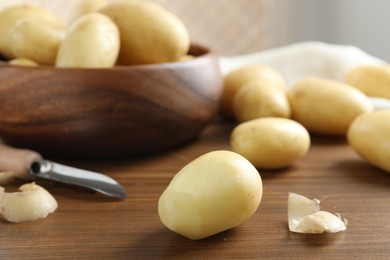 Fresh raw potatoes and peeler on wooden table, closeup