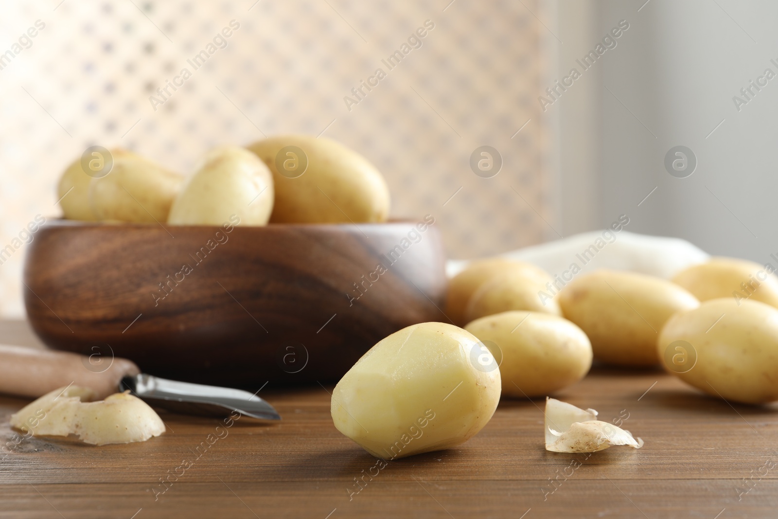 Photo of Fresh raw potatoes and peeler on wooden table, closeup