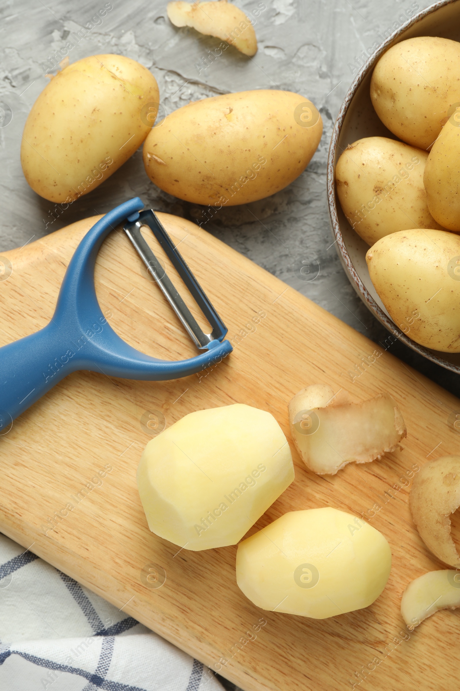 Photo of Fresh raw potatoes and peeler on grey table, flat lay