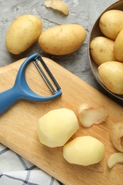 Photo of Fresh raw potatoes and peeler on grey table, flat lay