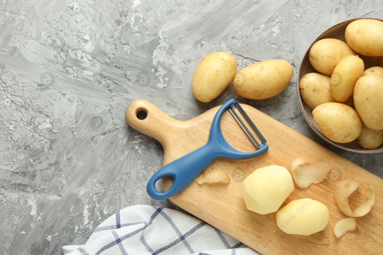 Photo of Fresh raw potatoes and peeler on grey table, flat lay. Space for text