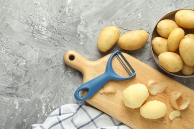 Fresh raw potatoes and peeler on grey table, flat lay. Space for text