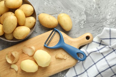 Photo of Fresh raw potatoes and peeler on grey table, flat lay