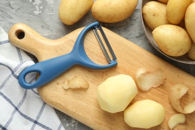 Fresh raw potatoes and peeler on grey table, flat lay