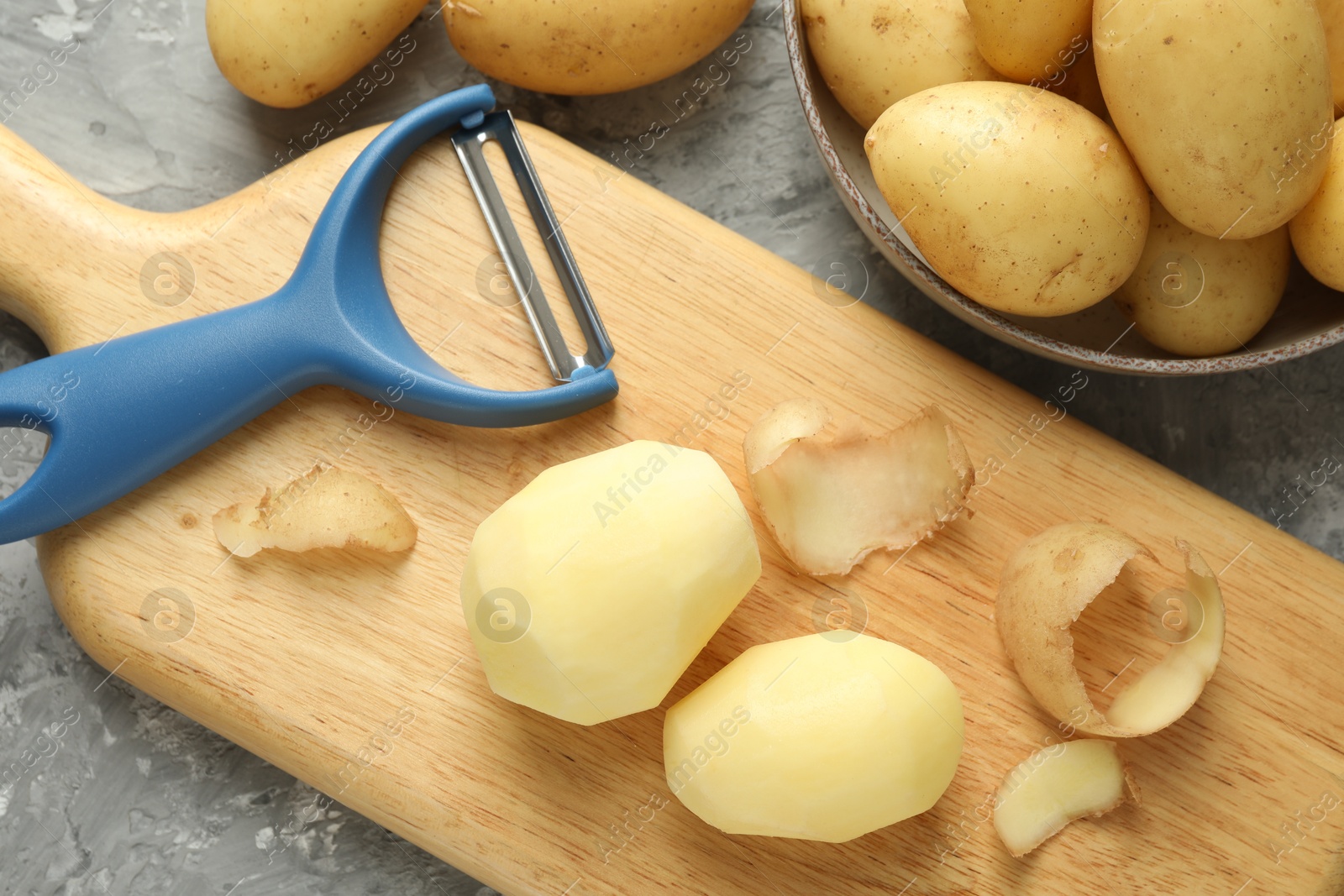 Photo of Fresh raw potatoes and peeler on grey table