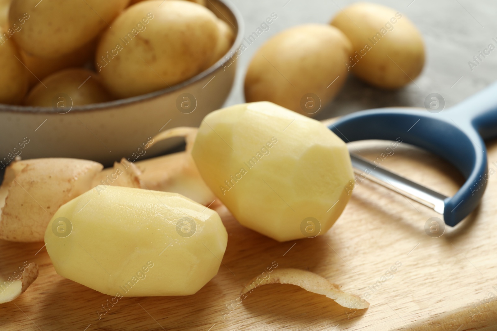 Photo of Fresh raw potatoes and peeler on table, closeup