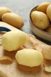 Fresh raw potatoes and peeler on table, closeup